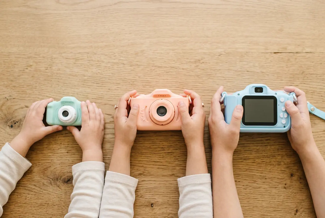 Trois mains d’enfants d’âges différents tenant chacune un appareil photo pour enfant